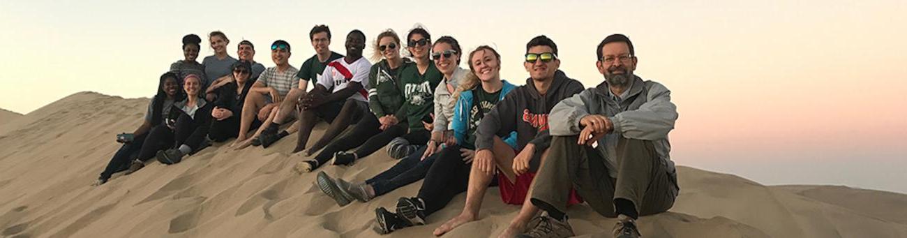 全球健康学院的学生和教职员工坐在沙丘上